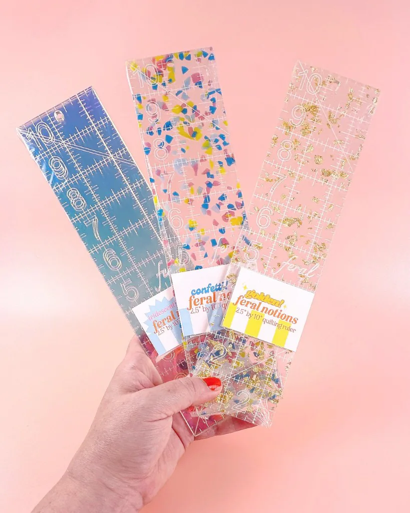 A hand holding three colorful quilting rulers